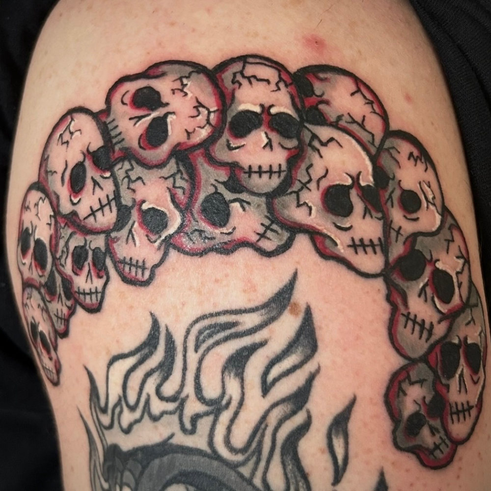 Pile of skulls tattoo with red linework and flames